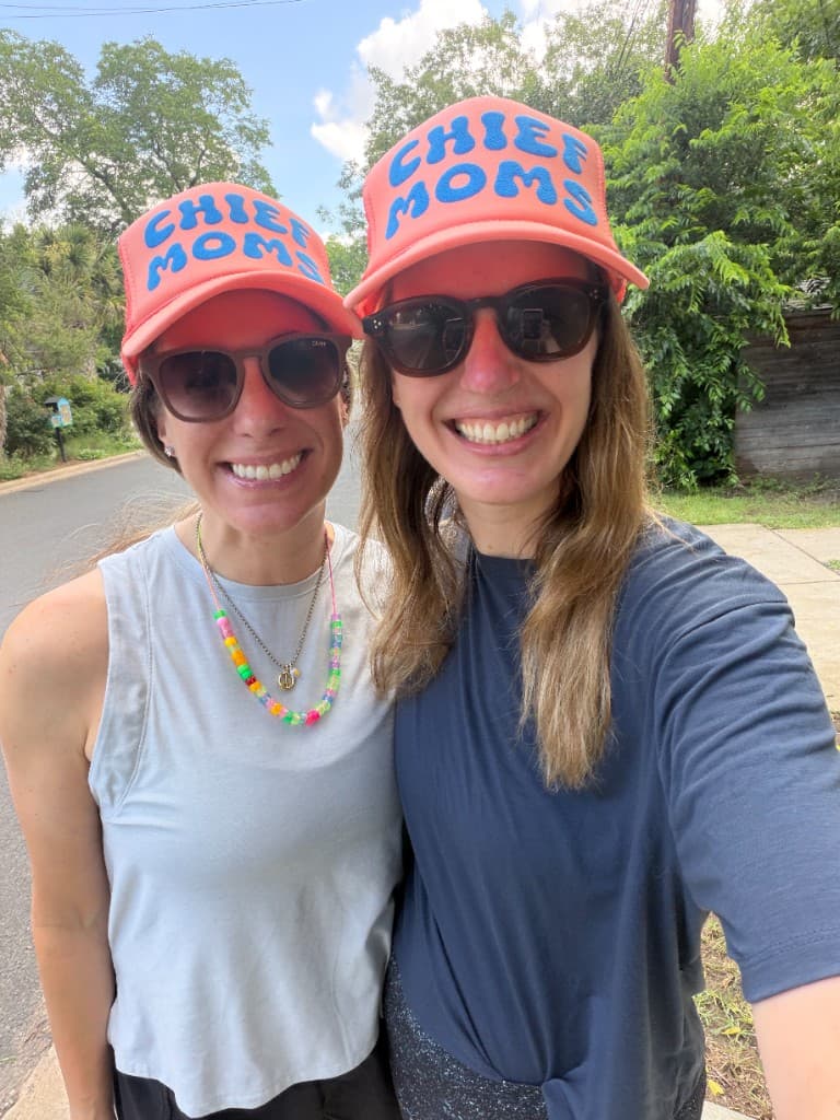 Two moms smiling on a Chief Moms walk wearing matching Chief Moms trucker hats