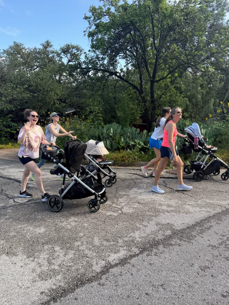 Moms walking together with strollers on a tree-lined path on a Saturday morning