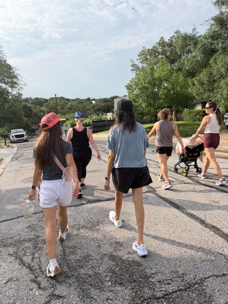 Moms walking together down a tree-lined Austin street on a Saturday morning, strollers welcome